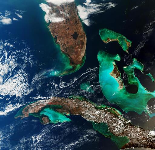 Questa immagine, catturata dalla missione Copernicus Sentinel-3, mostra in alto la punta meridionale della Florida, il circolare Lago Okeechobee che scende attraverso le Everglades e l'arcipelago curvilineo di isole noto come Florida Keys fino a Key West. Le acque circostanti, turchesi e blu profondo, creano un sorprendente richiamo alla bellezza e alla diversità del nostro pianeta, rendendo questa una scena appropriata per celebrare mille vedute della Terra dallo spazio.

In basso nell'immagine si trova Cuba, parzialmente velata da nuvole. L'area più scura e senza nuvole lungo la costa meridionale dell'isola è la Palude Zapata, la più grande zona umida di Cuba, che si estende attraverso la Penisola di Zapata e circonda la Baia dei Porci. La penisola si protende nelle acque turchesi del Golfo di Batabanò, che separa la terraferma cubana dalla circolare Isola della Gioventù.

Tra la Florida e Cuba si trova il banco di Cay Sal, che appare come una piccola area di acqua turchese nel blu scuro dello Stretto di Florida.

A est, possiamo vedere le Bahamas, che consistono in una catena di isole e banchi di acque poco profonde. L'isola più grande, Andros, si trova sul bordo orientale del Grande Banco delle Bahamas, una piattaforma sommersa poco profonda. Il contrasto tra le acque verdi e turchesi del banco e le più scure acque dell'Atlantico segna chiaramente la brusca transizione verso acque più profonde.